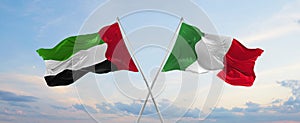 two crossed flags United Arab Emirates and Italy waving in wind at cloudy sky. Concept of relationship, dialog, travelling between
