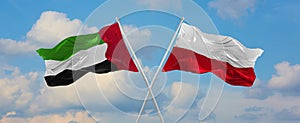 two crossed flags United Arab Emirates and Poland waving in wind at cloudy sky. Concept of relationship, dialog, travelling