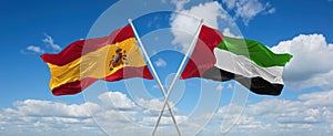 two crossed flags United Arab Emirates and spain waving in wind at cloudy sky. Concept of relationship, dialog, travelling between