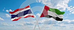 two crossed flags United Arab Emirates and Thailand waving in wind at cloudy sky. Concept of relationship, dialog, travelling