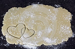 Two crossed hearts on dough layer flour powdered