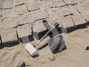 Two crossed rubber hammers lie on the unfinished laying of granite paving stones