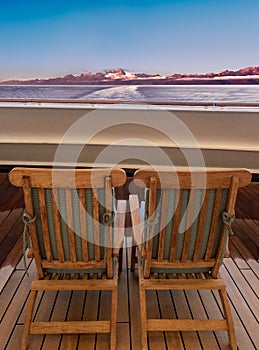 Two cruise ship wood lounge chairs facing sea and mountains at dawn, Alaska, USA