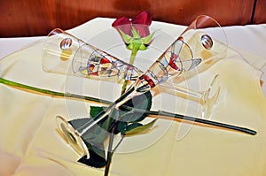 Two crystal glasses for champagne with a red rose on a tray.
