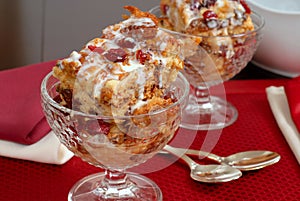 Two crystal goblets filled with Italian Panettone cranberry bread pudding with sauceboat in background