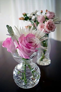 Two crystal vases filled with roses and other small flowers