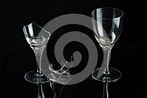 Two crystal wine glass and shattered glass on a black mirror background.