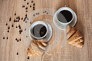 Two cup of hot coffee in a plate and a croissants. Coffee beans are scattered on a table