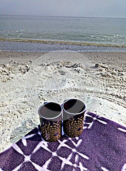 Two cups on a blanket on the beach.