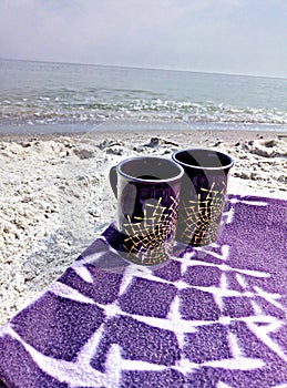 Two cups on a blanket on the beach.