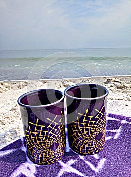 Two cups on a blanket on the beach.