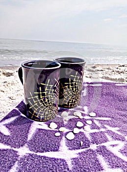 Two cups on a blanket on the beach.