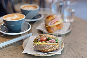 Two cups of cappuccino with latte art, sandwich and croissant on marble background. Concept of easy breakfast. Gray