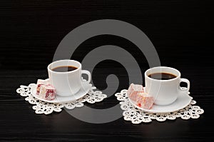 Two cups of coffee on the lace napkins and turkish dessert on a black background