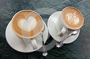 Two cups of coffee on a table with latte art heart and leaf