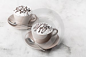 Two cups of coffee with whipped cream and chocolate topping. Iced frappuccino in white cup isolated on bright marble background. photo