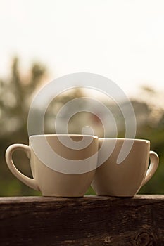 Two cups of coffee on wooden balcony on the background of sunset with beautiful bokeh lights