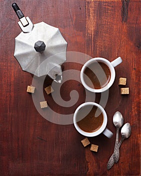 Two cups of espresso with pieces of cane sugar and Italian coffee maker.