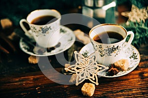 Two cups of espresso with pieces of cane sugar and Italian coffee maker on wooden table.