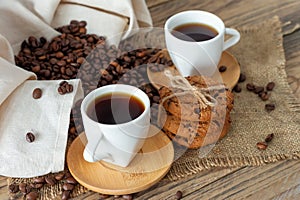 Two cups of freshly brewed espresso on wooden table. coffee beans and crunchie cookies on light wooden table  rustic style 