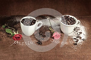Two cups full of coffee beans with red bud rose on wooden table.