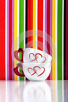 Two cups with hearts on colorful stripes background