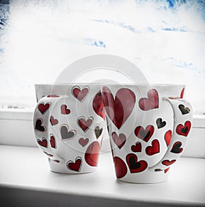 Two cups with hearts on the window sill of a frozen