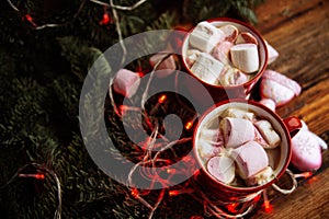 Two cups of hot chocolate with marshmallows and candy canes and red christmas malls on a dark wooden background. Place for text