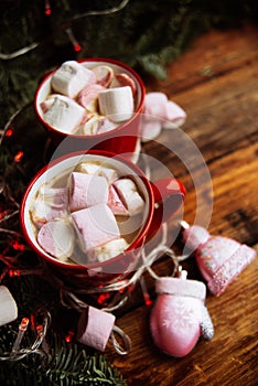 Two cups of hot chocolate with marshmallows and candy canes and red christmas malls on a dark wooden background. Place for text