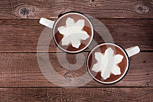 Two cups of hot chocolate with snowflake marshmallows, above view over a rustic wood