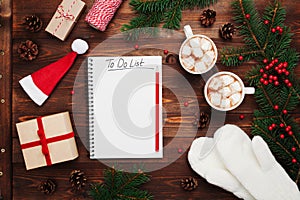 Two cups of hot cocoa or chocolate with marshmallow, gifts, mittens, christmas fir tree and notebook with to do list. Flat lay.