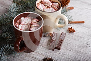 Two cups of sweet cocoa with marshmallows next to a pine branch on a table background. Winter hot chocolate.