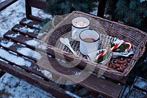 Two cups of hot cocoa in a wicker basket on a wooden table.