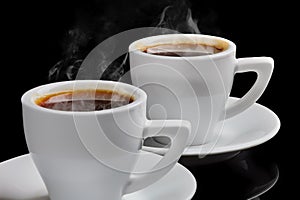 Two cups of hot coffee with steam on a black background