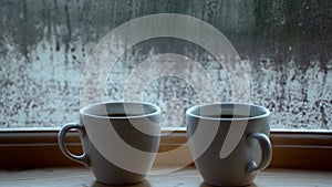 Two cups of hot drink coffee near window, water condensation on window glass, early morning, wake up concept