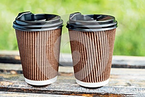 Two cups with hot drink to take away in park on wooden bench.