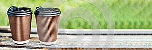 Two cups with hot drink to take away in park on wooden bench.