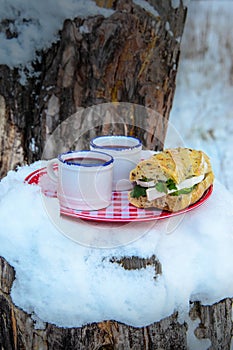 Two cups of hot mulled wine on a plate in a snowy forest