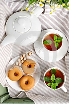 Two cups of hot tea with delicious cookies on white wooden table