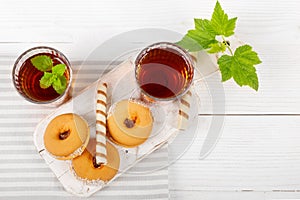 Two cups of hot tea with delicious cookies on white wooden table