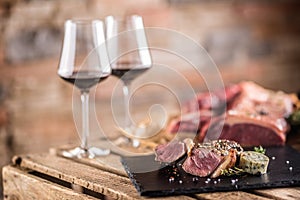 Two cups with red wine roasted and raw beef steak on slate board