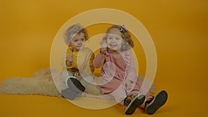 Two curly smiling kids sitting on carpet with lollipops