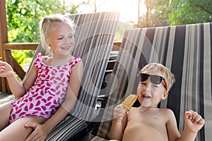 Two cute adorable caucasian blond little siblings enjoy having fun relaxing and eat fruit popsicle icecream sitting on