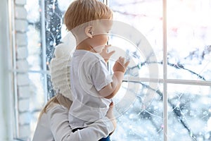 Two cute adorable little blond cauasian children siblings stay near window and looking outside waiting for snow, wonders photo