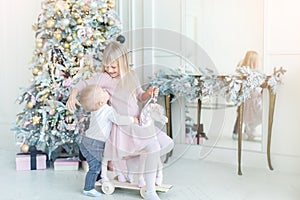 Two cute adorable little siblings brother and sister having fun playing with retro wooden wheel horse toy near christmas tree in