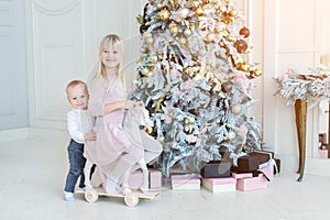 Two cute adorable little siblings brother and sister having fun playing with retro wooden wheel horse toy near christmas tree in