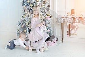 Two cute adorable little siblings brother and sister having fun playing with retro wooden wheel horse toy near christmas