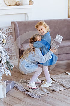 Two cute adorable little sisters near christmas tree in cozy living room.