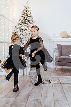 Two cute adorable little sisters near christmas tree in cozy living room.