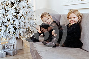 Two cute adorable little sisters near christmas tree in cozy living room.